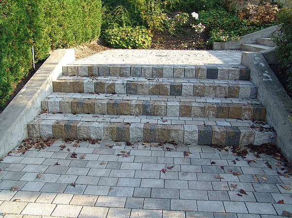 Concrete block steps with mixed-tone risers and coordinated paving stones in a landscaped garden path.
